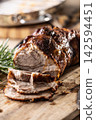 Detailed macro shot of juicy roasted pork shoulder with a perfectly browned crust. Tender meat slices lie on a wooden board next to fragrant rosemary, creating an inviting composition for any gourmet 142594451