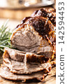Detailed macro shot of juicy roasted pork shoulder with a perfectly browned crust. Tender meat slices lie on a wooden board next to fragrant rosemary, creating an inviting composition for any gourmet 142594453