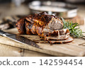 Tasty roasted pork neck with a crispy crust is garnished with fresh rosemary and sliced on a wooden board. This professional culinary shot will fit perfectly in cookbooks, restaurant menus, or food 142594454