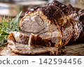 Tasty roasted pork neck with a crispy crust is garnished with fresh rosemary and sliced on a wooden board. This professional culinary shot will fit perfectly in cookbooks, restaurant menus, or food 142594456