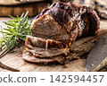 Tasty roasted pork neck with a crispy crust is garnished with fresh rosemary and sliced on a wooden board. This professional culinary shot will fit perfectly in cookbooks, restaurant menus, or food 142594457