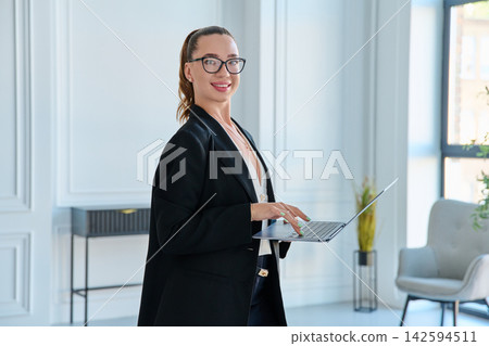 Smiling businesswoman in glasses holding open laptop in office Smiling businesswoman in glasses holding open laptop in office 142594511