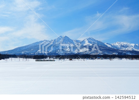 A scene of a train traveling near Sekiyama Station on the Myoko Hanema Line, with Mount Myoko in the background during winter. 142594512