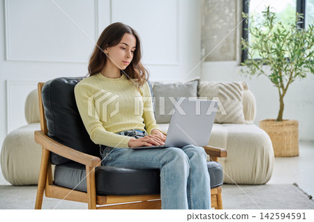 Young 18 years old woman using laptop in armchair at home Young 18 years old woman using laptop in armchair at home 142594591