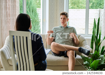 Teenage boy talking to female therapist during counseling session in office 142594630