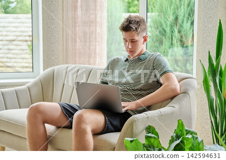 Teenage boy using laptop while sitting on sofa at home Teenage boy using laptop while sitting on sofa at home 142594631