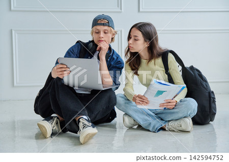 Two focused teenage students looking at laptop screen while studying together on floor Two focused teenage students looking at laptop screen while studying together on floor 142594752