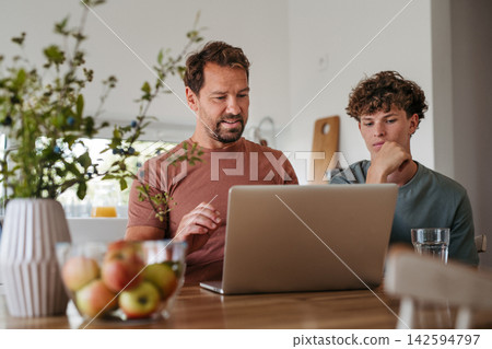 Father supporting teen son with online learning at home. Father supporting teen son with online learning at home. 142594797