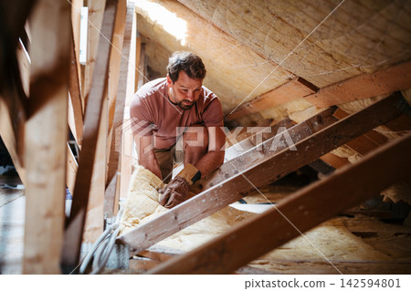 Homeowner insulating attic during home renovation project. Homeowner insulating attic during home renovation project. 142594801