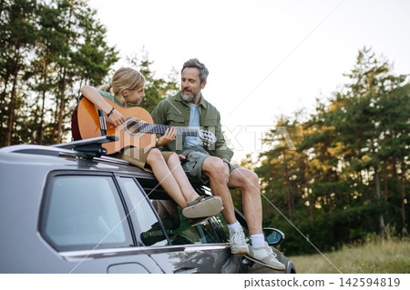 Dad teaching boy how to play guitar during summer camping adventure in nature. 142594819