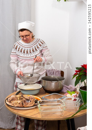 A woman stands in her kitchen preparing kholodets, aspic, a traditional Ukrainian dish. She strains the broth from the bones into a bowl while wearing comfortable clothes A woman stands in her kitchen preparing kholodets, aspic, a traditional Ukrainian dish. She strains the broth from the bones into a bowl while wearing comfortable clothes 142595215