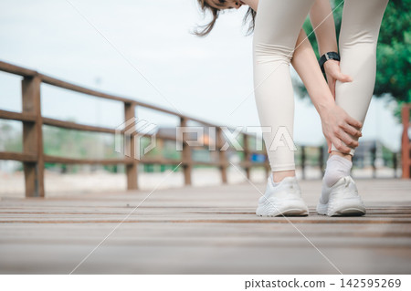 Female runner with achilles tendon injury holds painful lower leg, suffering from sudden calf muscle strain or ankle sprain during outdoor training on wooden boardwalk Female runner with achilles tendon injury holds painful lower leg, suffering from sudden calf muscle strain or ankle sprain during outdoor training on wooden boardwalk 142595269