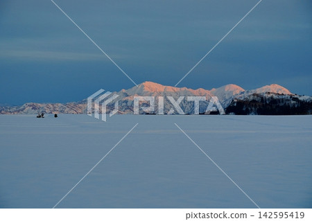 A view of the Echigo Sanzan mountains bathed in the setting sun, with a snowfield in the foreground, as seen from Ikegahara, Ojiya City. Ver2 142595419