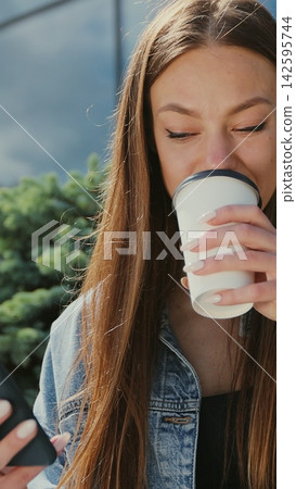 Vertical video. smiling woman typing message near office building during coffee break. Girl using smartphone and drinking coffee on the street bench. Vertical video. smiling woman typing message near office building during coffee break. Girl using smartphone and drinking coffee on the street bench. 142595744