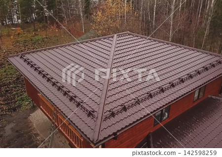 House with a brown metal roof.Corrugated metal roof and metal roofing. Modern roof made of metal. House with a brown metal roof.Corrugated metal roof and metal roofing. Modern roof made of metal. 142598259