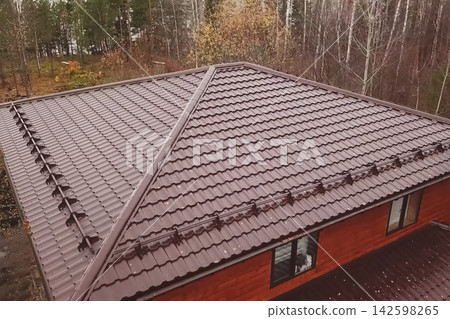 House with a brown metal roof.Corrugated metal roof and metal roofing. Modern roof made of metal. House with a brown metal roof.Corrugated metal roof and metal roofing. Modern roof made of metal. 142598265