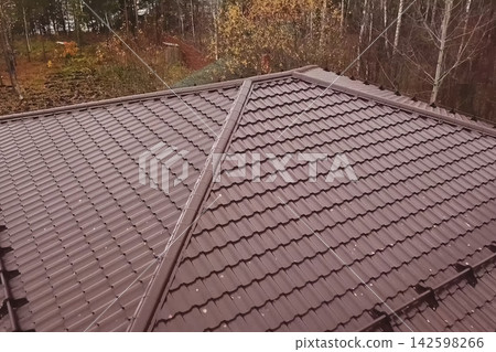 House with a brown metal roof.Corrugated metal roof and metal roofing. Modern roof made of metal. House with a brown metal roof.Corrugated metal roof and metal roofing. Modern roof made of metal. 142598266