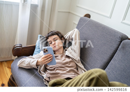 Lazy young zoomer woman scrolling smartphone lying on sofa, distracted by digital addiction at home Lazy young zoomer woman scrolling smartphone lying on sofa, distracted by digital addiction at home 142599816