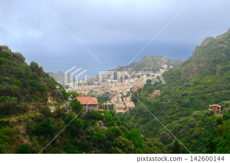 charming coastal town with terracotta roofs cascades down verdant slopes towards the blue ocean under a misty sky charming coastal town with terracotta roofs cascades down verdant slopes towards the blue ocean under a misty sky 142600144