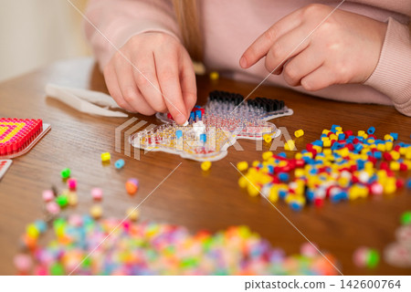 Child creating colorful bead art at a wooden table during a fun creative craft activity Child creating colorful bead art at a wooden table during a fun creative craft activity 142600764