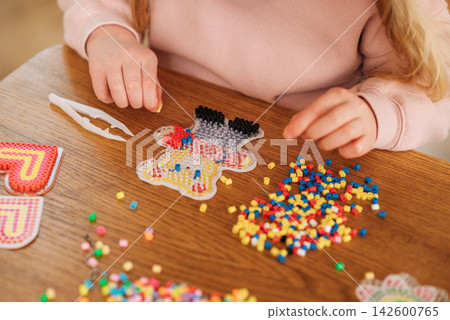 Child creating colorful bead art at a wooden table during a fun creative craft activity Child creating colorful bead art at a wooden table during a fun creative craft activity 142600765