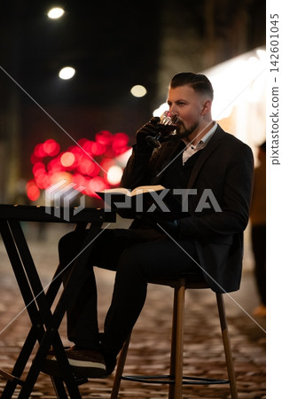 Evening relaxation with a book and drink in a vibrant urban setting adorned with festive lights and a cozy atmosphere during a night out Evening relaxation with a book and drink in a vibrant urban setting adorned with festive lights and a cozy atmosphere during a night out 142601045