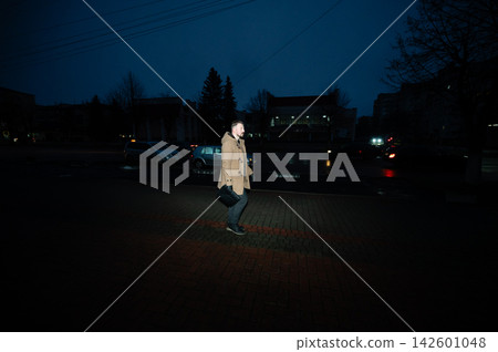 Man walks through a dark urban environment on a chilly evening, illuminated by streetlights and the glow of passing cars as the day gives way to night Man walks through a dark urban environment on a chilly evening, illuminated by streetlights and the glow of passing cars as the day gives way to night 142601048