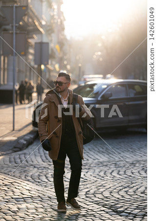 Stylish man strolling on cobblestone street in the golden light of sunset, showcasing urban elegance on a chilly afternoon in the city Stylish man strolling on cobblestone street in the golden light of sunset, showcasing urban elegance on a chilly afternoon in the city 142601049