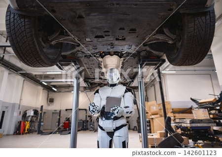 A humanoid robot with a tablet and wrench stands beneath a car on a lift in a modern garage setting A humanoid robot with a tablet and wrench stands beneath a car on a lift in a modern garage setting 142601123
