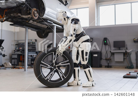 A humanoid robot is shown in a garage, holding a car tire while a vehicle is lifted on a hydraulic lift for repairs A humanoid robot is shown in a garage, holding a car tire while a vehicle is lifted on a hydraulic lift for repairs 142601148