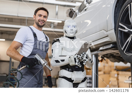 A smiling mechanic holding a tool stands next to a humanoid robot with a tablet in a car repair garage 142601176