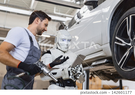 A human mechanic collaborates with a humanoid robot on a car repair, discussing diagnostics on a tablet A human mechanic collaborates with a humanoid robot on a car repair, discussing diagnostics on a tablet 142601177