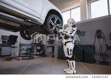 A humanoid robot is performing maintenance on a car's wheel in a modern garage setting A humanoid robot is performing maintenance on a car's wheel in a modern garage setting 142601197