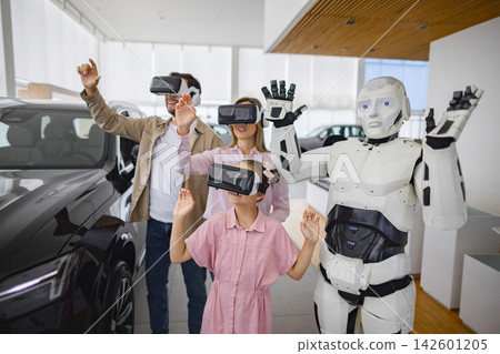 A family and a humanoid robot interact with virtual reality headsets in a modern car dealership environment 142601205