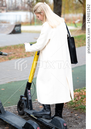 Enjoying a sunny afternoon, a stylish individual checks a scooter in a vibrant urban park surrounded by autumn leaves and lively pathways Enjoying a sunny afternoon, a stylish individual checks a scooter in a vibrant urban park surrounded by autumn leaves and lively pathways 142601262