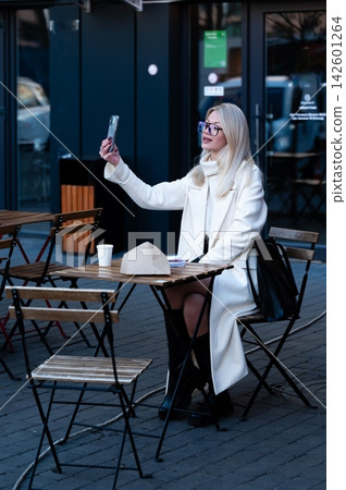 Capturing a moment of joy while sitting at an outdoor cafe in the city as the afternoon sun creates a warm glow around the stylish woman enjoying her coffee Capturing a moment of joy while sitting at an outdoor cafe in the city as the afternoon sun creates a warm glow around the stylish woman enjoying her coffee 142601264