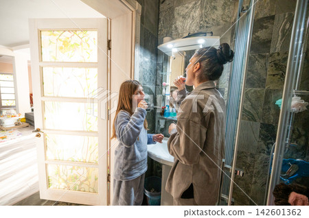 A delightful morning routine unfolds in a cozy bathroom, where both a child and an adult enjoy the warmth of natural light streaming in A delightful morning routine unfolds in a cozy bathroom, where both a child and an adult enjoy the warmth of natural light streaming in 142601362