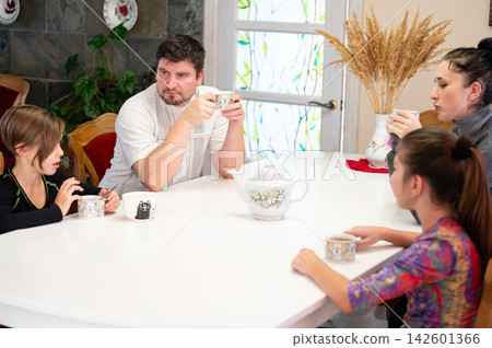Family gathering at a bright dining table sharing warm drinks and laughter during a cozy afternoon in a comfortable living space Family gathering at a bright dining table sharing warm drinks and laughter during a cozy afternoon in a comfortable living space 142601366