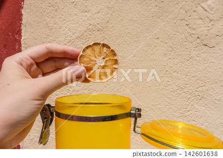 Hand Holding a Dried Lemon Slice with a Yellow Jar on a Red and Creamy Neutral Background Hand Holding a Dried Lemon Slice with a Yellow Jar on a Red and Creamy Neutral Background 142601638
