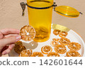 Hand Holding a Dried Lemon Slice with Jar and Plate of Dried Citrus 142601644