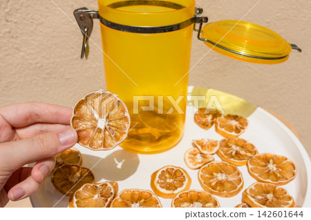 Hand Holding a Dried Lemon Slice with Jar and Plate of Dried Citrus Hand Holding a Dried Lemon Slice with Jar and Plate of Dried Citrus 142601644