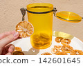 Hand Holding a Dried Lemon Slice with Jar and Plate of Dried Citrus 142601645