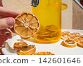 Hand Holding a Dried Lemon Slice with Jar and Plate of Dried Citrus 142601646