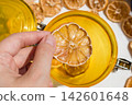 Hand Holding a Dried Lemon Slice with Jar and Plate of Dried Citrus 142601648