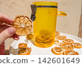 Hand Holding a Dried Lemon Slice with Jar and Plate of Dried Citrus 142601649