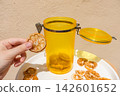 Hand Holding a Dried Lemon Slice with Jar and Plate of Dried Citrus 142601652