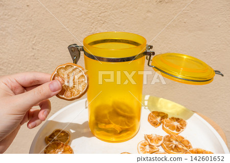 Hand Holding a Dried Lemon Slice with Jar and Plate of Dried Citrus Hand Holding a Dried Lemon Slice with Jar and Plate of Dried Citrus 142601652