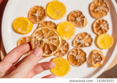 Hand Holding a Dried Lemon Slice Over a Plate of Fresh and Dried Lemon Slices Hand Holding a Dried Lemon Slice Over a Plate of Fresh and Dried Lemon Slices 142601655