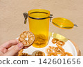 Hand Holding a Dried Lemon Slice with Jar and Plate of Dried Citrus 142601656