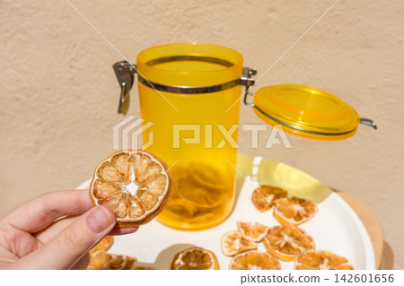 Hand Holding a Dried Lemon Slice with Jar and Plate of Dried Citrus Hand Holding a Dried Lemon Slice with Jar and Plate of Dried Citrus 142601656